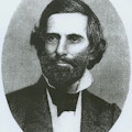 Howe with dark suit, white shirt with high collar, beard and mustache