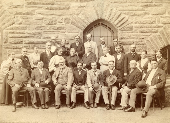 Attendees of the American Association To Promote Teaching Speech To The Deaf meeting held in 1896. Attendees pose for photograph in front of a stone building.