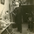 Alexander Graham Bell, standing indoors, looking at camera, surrounded by potted plants.