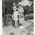 Two women and aboy in shorts standing on a sidewalk.