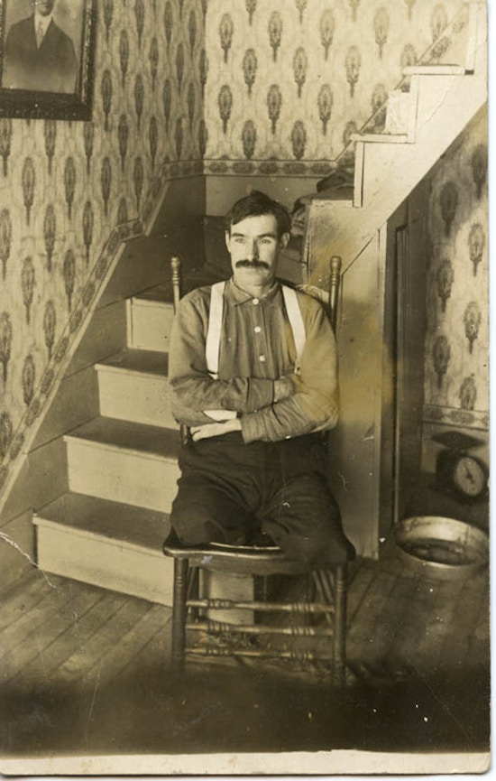 A man, a double-leg amputee, sits in chair, next to stairs.