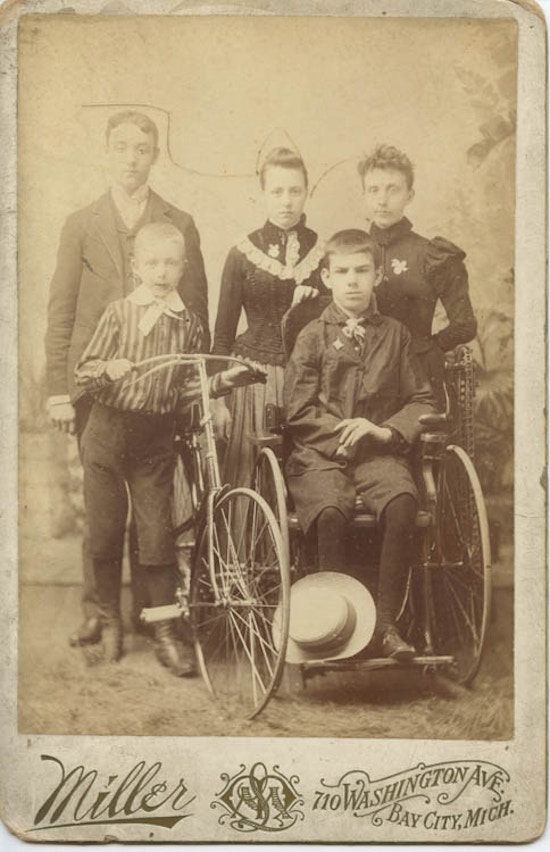 Portrait of family. One boy uses a wheelchair.  Another poses with his bicycle.