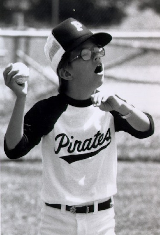 A with glasses wearing a baseball uniform prepares to throw a baseball.