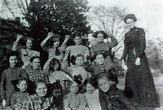A group of younger students with their teacher pose outdoors.  Four of the girls finger spell "Alabama"
