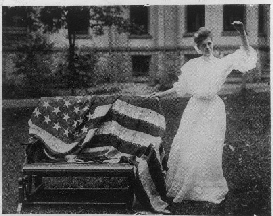 A woman signs next a flag draped over a bench.