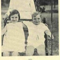 Two children sit in a swing with a nurse standing behind them.