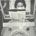 A woman in an iron lung reads a book using a mouthstick.