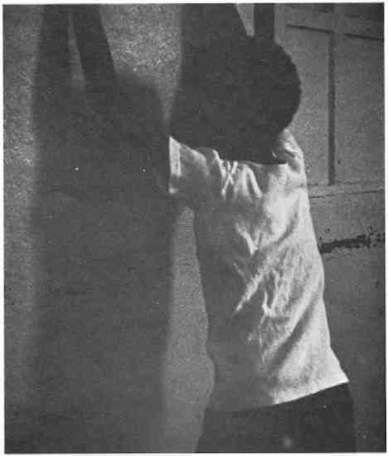 A young African-American man with his hands up on a wall.