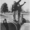 Three boys near large pipes, two saluting.