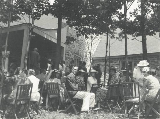 Group sitting on chairs next to Top Cottage porch.  A line of people leads to porch entrance.