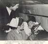 A man with a respirator attended by a nurse on a plane.