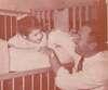 A smiling father plays with a young girl in a crib.
