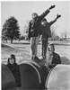 Three boys near large pipes, two saluting.