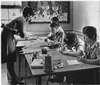 A woman helping four children working on art.
