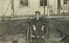 Photograph of a boy using a wheelchair in the yard of a small house.
