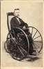 A man, with a hat on his lap, sits in a wheelchair.