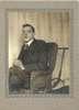 A young man with glasses sits in a wheelchair made of wicker.