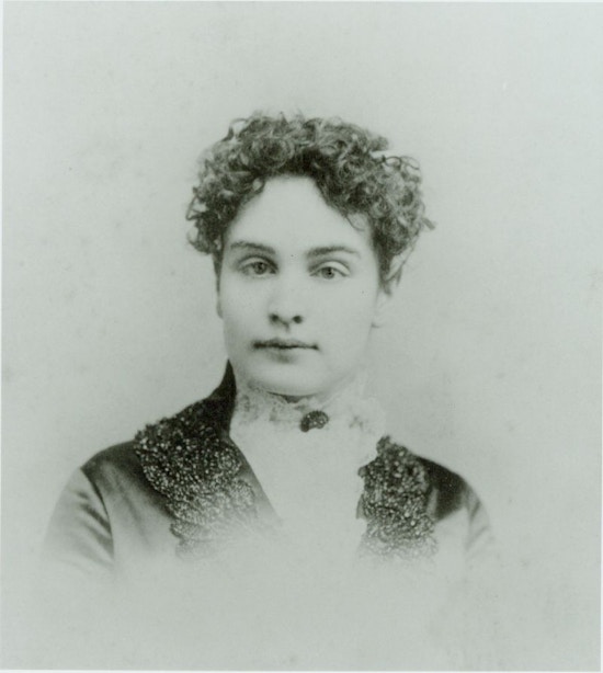 Young Sullivan facing camera, curly hair, dark dress, white lace collar with dark broach at throat.
