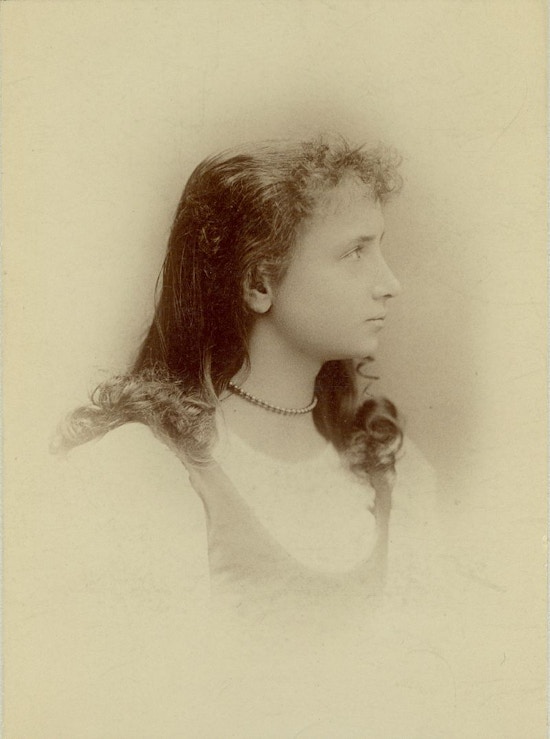 Young Helen Keller, side view looking right, white dress, necklace, hair down loosely arranged.