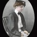 Helen Keller in her graduation gown, seated, facing right, colored.