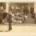 Behind the scene photograph of the group photograph of the first summer American Association To Promote Teaching Speech To The Deaf meeting taken on a Lake George porch with Alexander G. Bell. Photographer and camera are positioned left with the meeting participants in the background.