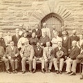 Attendees of the American Association To Promote Teaching Speech To The Deaf meeting held in 1896. Attendees pose for photograph in front of a stone building.