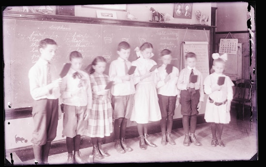 Both male and female deaf children stand in front of a chalk board to read at the Horace Mann School.