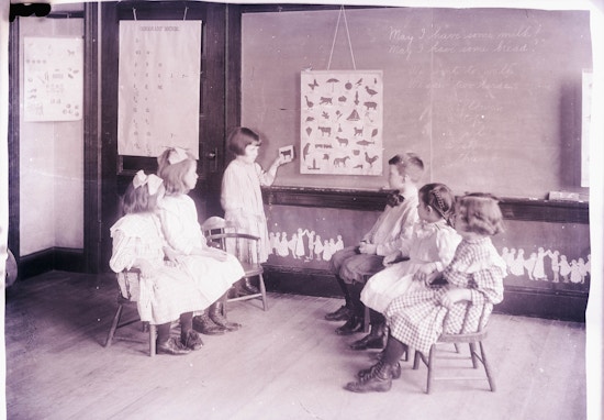 One student standing at the chalkboard and five students in the classroom sitting at the Horace Mann School.