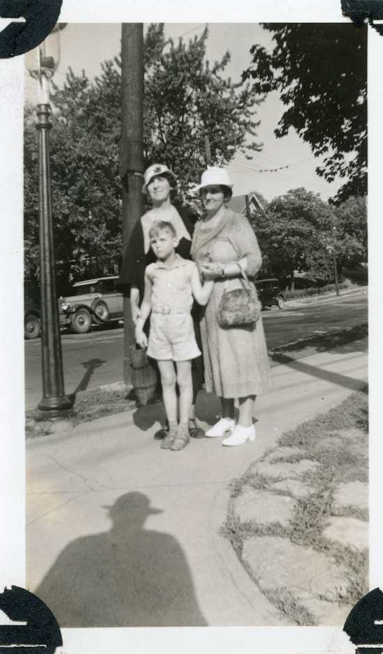 Two women and aboy in shorts standing on a sidewalk.