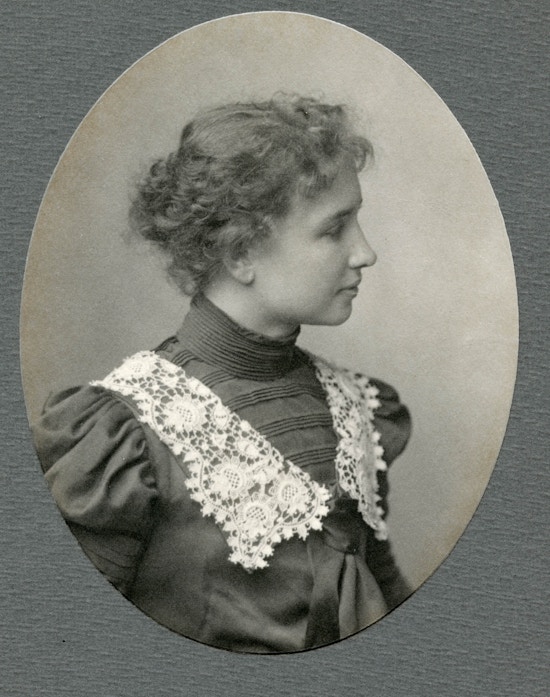 Helen Keller wearing lace collared dress with hair in a bun facing right in a head and shoulders portrait.