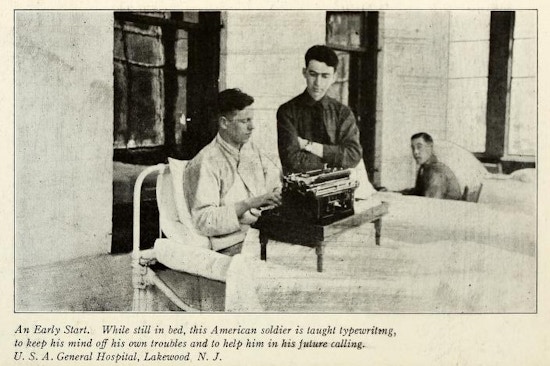 Man in bed uses typewriter while man in uniform looks on.