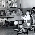Seven children sit at a table.  Three of the children have Down Syndrome.