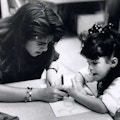 A teacher helps a young girl write her name.