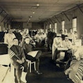 Photograph of ward in military hospital, including veterans, nurses, and doctors.  Several men use wheelchairs.