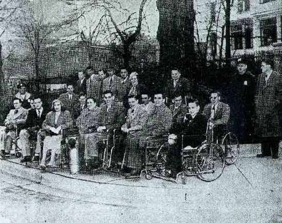 A newspaper photograph of about twenty people, about half of whom are in wheelchairs.