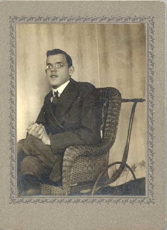 A young man with glasses sits in a wheelchair made of wicker.
