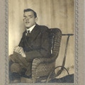 A young man with glasses sits in a wheelchair made of wicker.