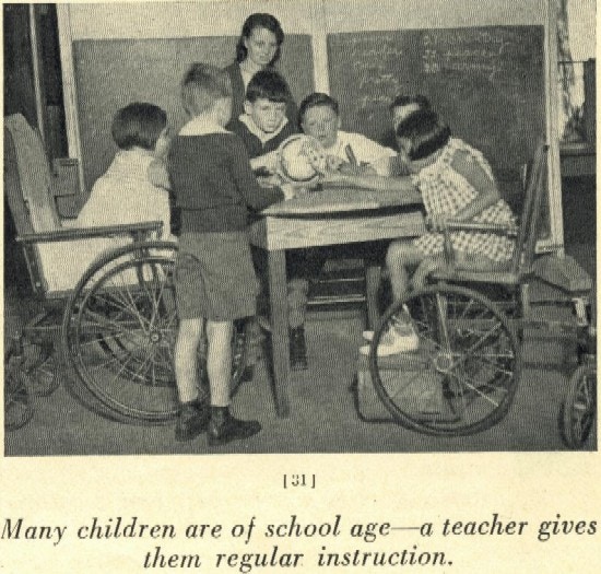 Six children, two in wheelchairs, examine a globe, their teacher in the background.