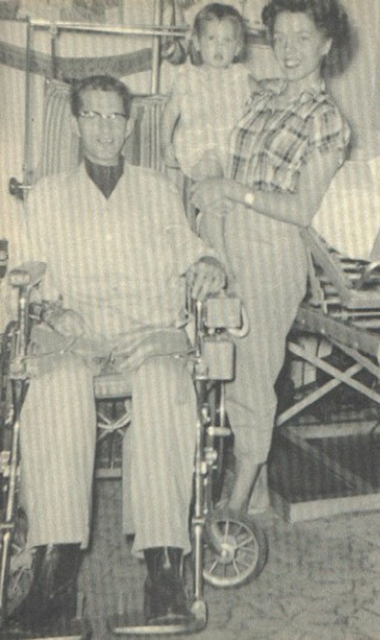 A young man in a wheelchair with his wife and young daughter.