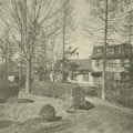 A house with circular driveway, tress, and shrubbery.