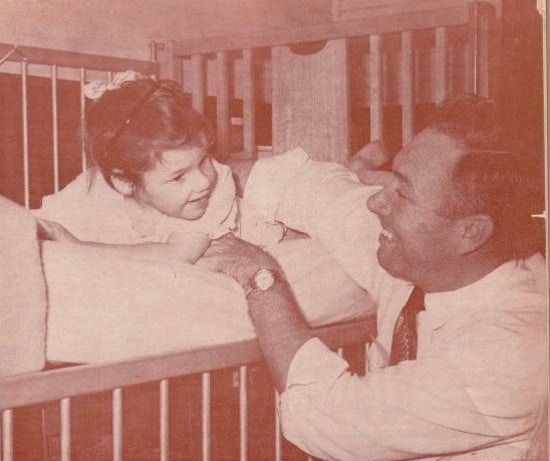 A smiling father plays with a young girl in a crib.