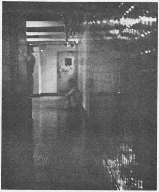 A man sitting on the floor at the end of a hall.