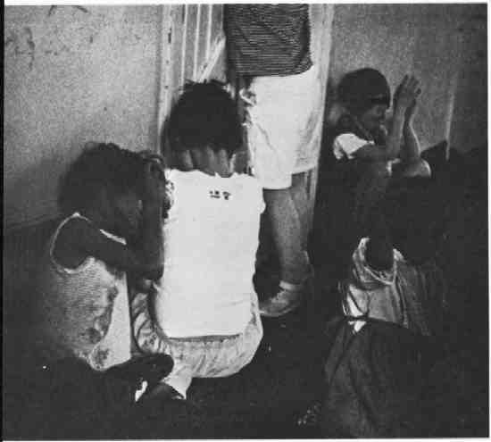 Children sitting on a floor in a dilapidated room.